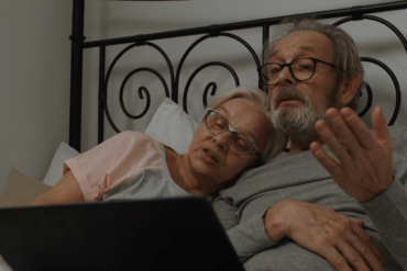 Old couple in bed using laptop.