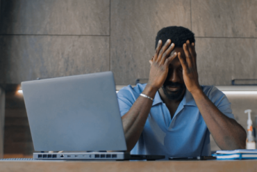 Stressed man with face in hands using a laptop.